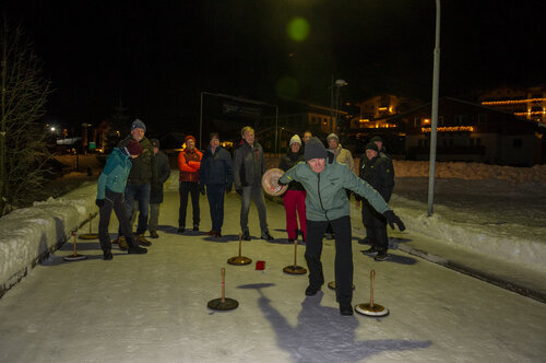 Gruppe beim Eisstockschießen auf einer beleuchteten Eisbahn am Winterabend in Viehhofen, umgeben von Schnee. | © viehhofen.at, Der Fotoigel