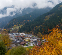 Blick auf Viehhofen im herbstlichen Glemmtal mit bunt gefärbten Bäumen, bewaldeten Berghängen und tief hängenden Wolken über dem Ort. | © viehhofen.at, Der Fotoigel