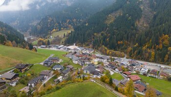 Luftaufnahme von Viehhofen im herbstlichen Glemmtal mit Wohnhäusern, grünen Wiesen und bunt gefärbten Wäldern an den umliegenden Berghängen. | © viehhofen.at, Der Fotoigel