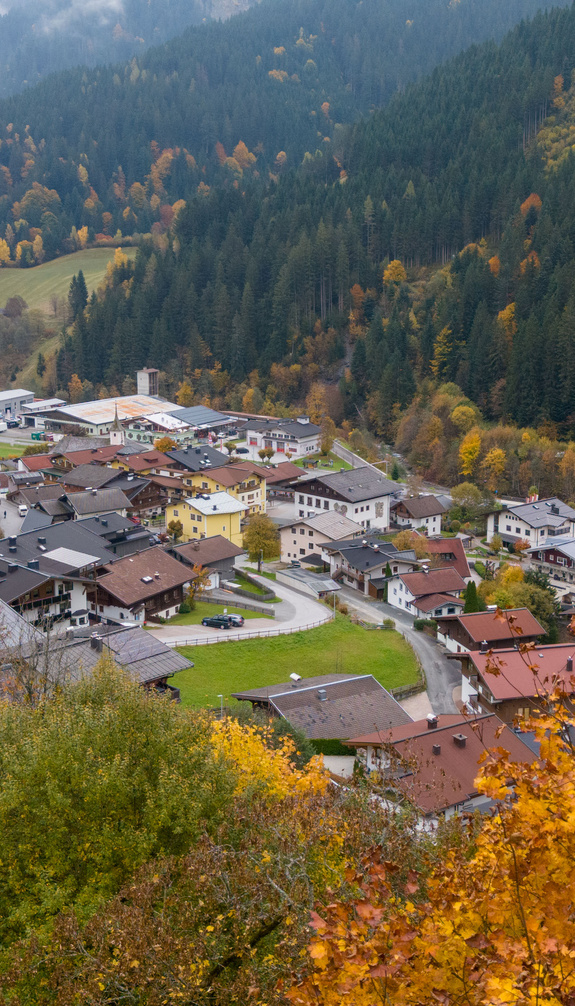 Blick auf Viehhofen im herbstlichen Glemmtal mit Häusern im Ortszentrum, bunt gefärbten Bäumen und bewaldeten Berghängen. | © viehhofen.at, Der Fotoigel