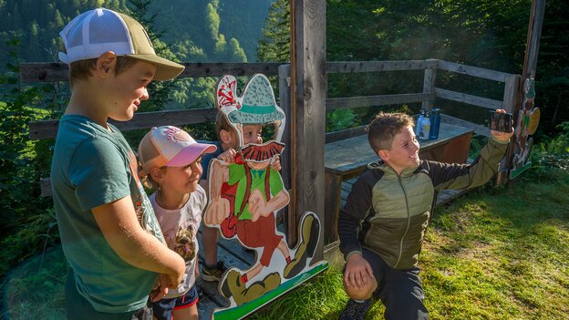 Drei Kinder an einer Wander-Nik-Erlebnisstation in Viehhofen, während eines mit dem Smartphone ein gemeinsames Foto mit der Wander-Nik-Figur aufnimmt. | © viehhofen.at, Der Fotoigel