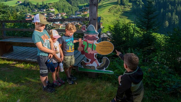 Kinder am Wander-Nik Fotopoint in Viehhofen mit Wander-Nik-Figur und Blick auf den Ort sowie die grüne Berglandschaft. | © viehhofen.at, Der Fotoigel