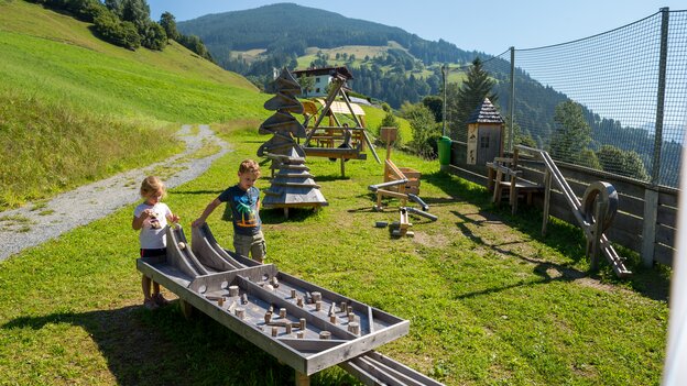 Zwei Kinder spielen an einer großen Kugelbahn-Spielstation in Viehhofen, umgeben von Wiesen und weiteren Spielelementen in der grünen Berglandschaft. | © viehhofen.at, Der Fotoigel