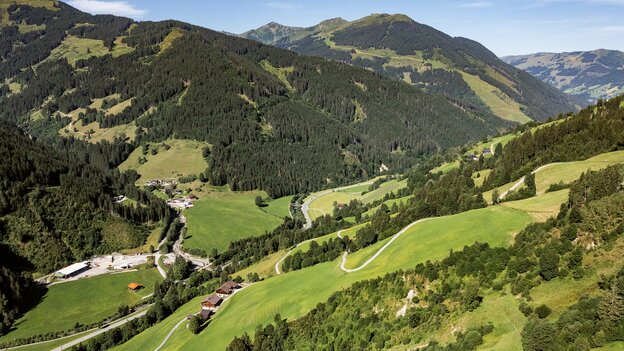 Weiter Panoramablick über die grüne Berglandschaft rund um Viehhofen mit Wiesen, bewaldeten Hängen, verstreuten Häusern und kurvenreichen Straßen im Glemmtal. | © viehhofen.at, Amido