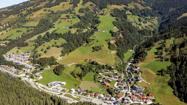 Luftaufnahme von Viehhofen im Sommer mit dem Ortsgebiet im Tal, grünen Wiesen, bewaldeten Berghängen und der umliegenden Berglandschaft im Glemmtal. | © viehhofen.at, Amido