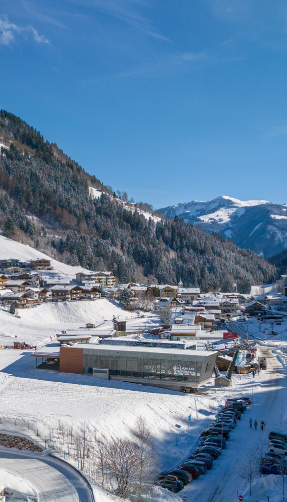 Winter view of Viehhofen with the zellamseeXpress, snow-covered valley, houses, mountain road and forested slopes in the Glemmtal. | © viehhofen.at, Der Fotoigel