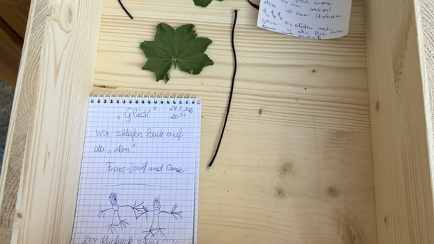 Geöffnete Holzbox am Glücksweg in Viehhofen mit handgeschriebenen Glücksbotschaften, Zeichnungen und gesammelten Blättern. | © viehhofen.at