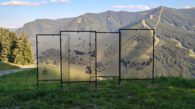 Perspektiven-Figur am Glücksweg in Viehhofen mit mehreren transparenten Bildtafeln und gezeichneten Naturmotiven vor der umliegenden Berglandschaft. | © viehhofen.at