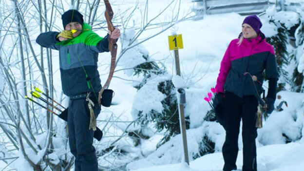 Two people on the snowy archery course in Viehhofen, while one person aims with a bow and arrow at a target. | © Der Fotoigel