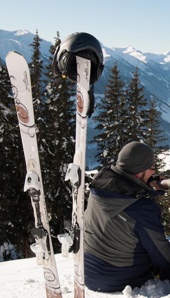 Couple sitting in the snow on the mountain with skis in the foreground | © viehhofen.at